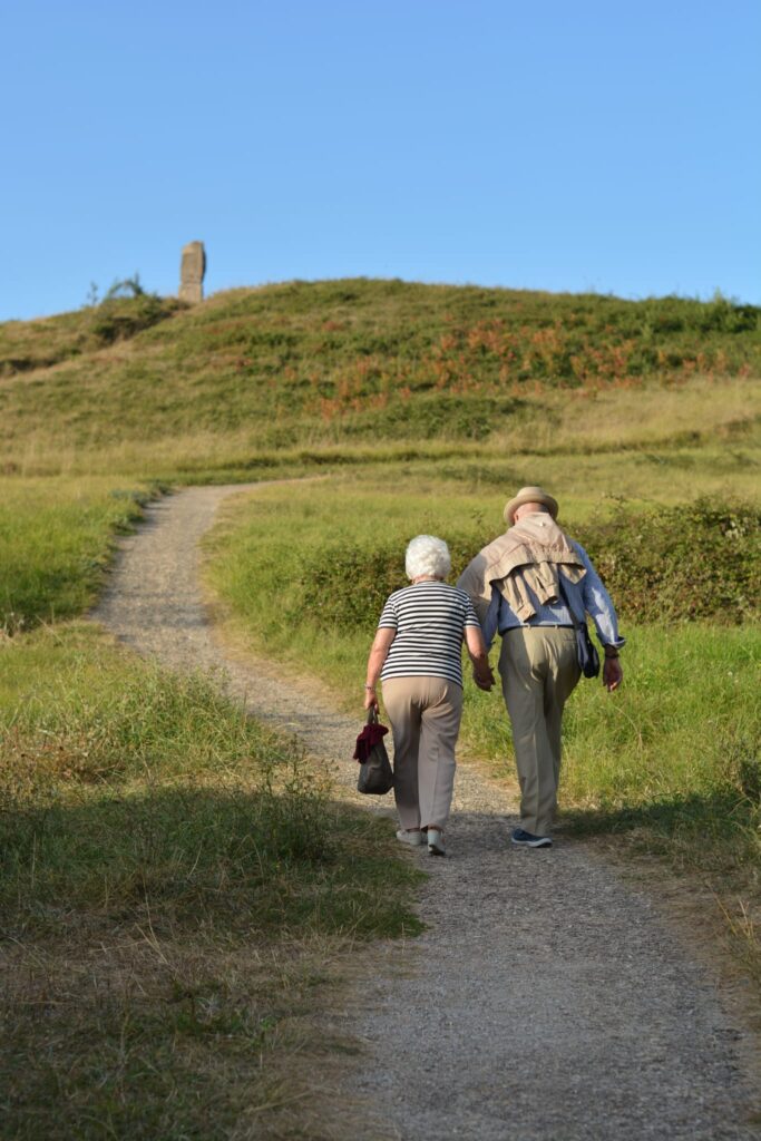 Un hombre y una mujer de avanzada edad caminando de la mano por la ladera de una montana.